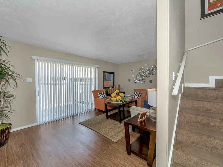 Spacious living room with wood-style flooring, large sliding glass doors for natural light, and townhome-style staircase at Watersong Villas Apartments.