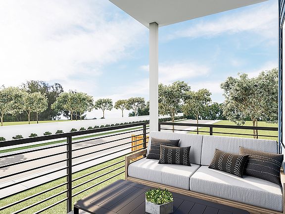 A balcony with a comfortable sofa and decorative pillows, overlooking a lush green landscape with tr