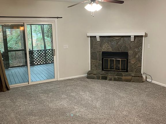 Living room with stone fireplace and screened porch leading to wooded lot.