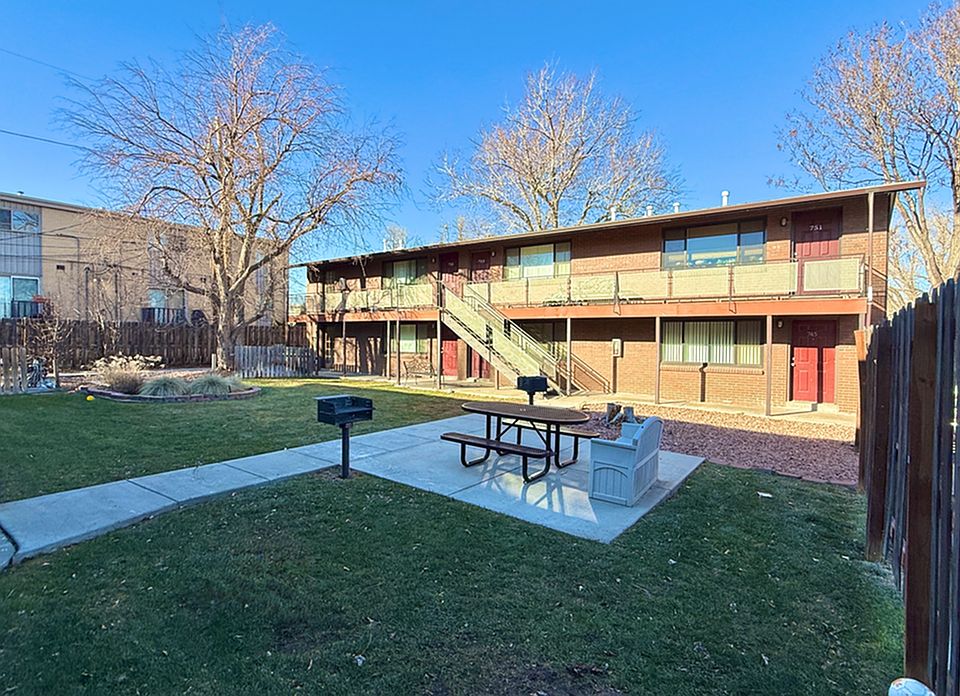 Cozy apartment complex with charming red doors and an inviting courtyard featuring a picnic area and barbecue spot, surrounded by lush greenery.