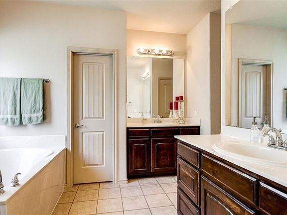 Master bath has his and her walk in wardrobe closets, his and her vanities, garden tub, separate shower, tile floors, stained custom cabinets, private toilet.