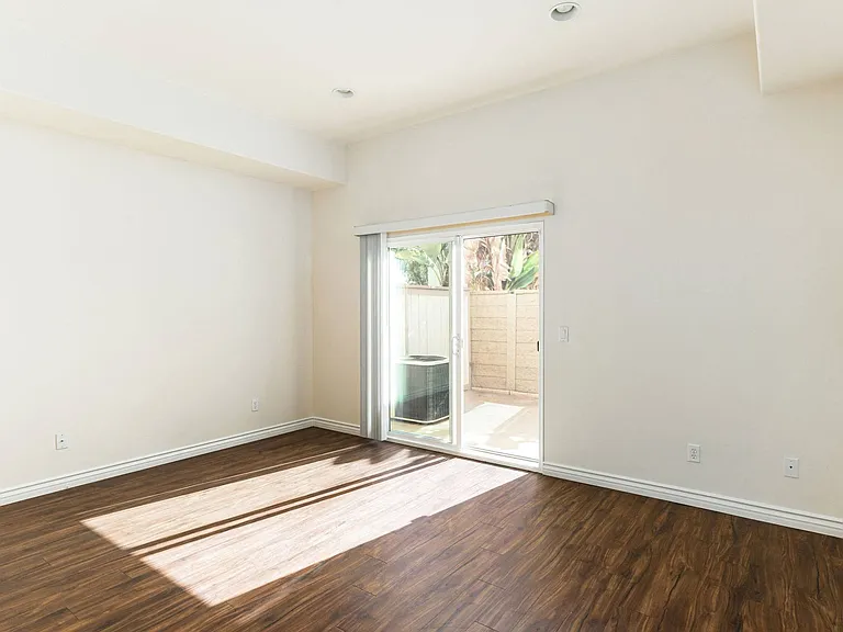 Living room with wood style laminate floors and sliding glass doors to private porch at The Nines Townhomes in Escondido, California.