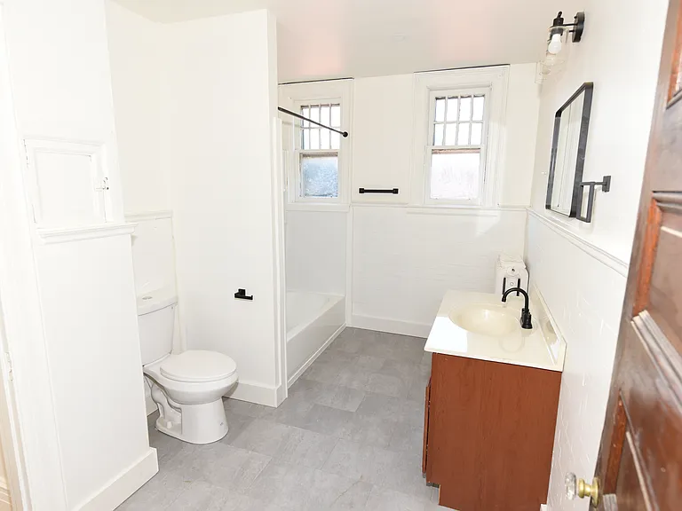 Bright, updated bathroom featuring a full tub-and-shower combination, white tile surround, built-in shower niche, modern black fixtures, and easy-to-maintain flooring