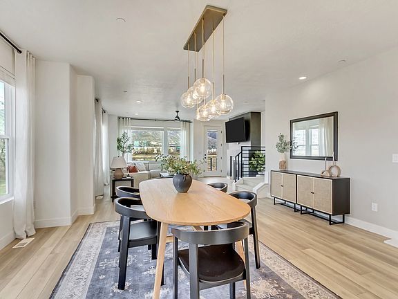 A modern dining room features a wooden table with black chairs, a decorative rug, hanging pendant li