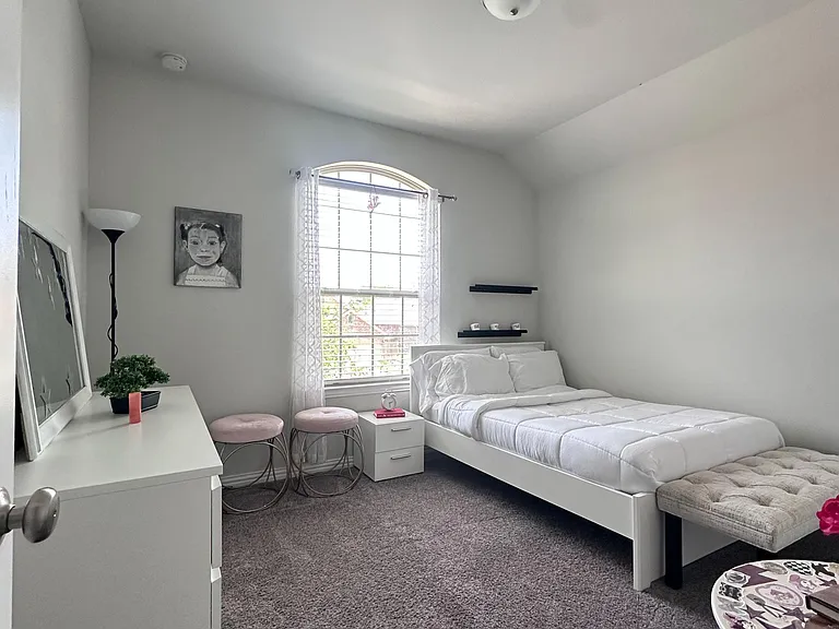 Private bedroom with plush carpet, arched window, and a simple layout for a bed plus desk or storage.