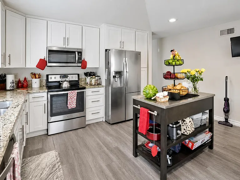 Updated kitchen with white cabinetry, granite counters, stainless appliances, and a movable island for added prep space.