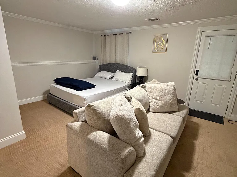 Furnished bedroom featuring a full bed, sitting area, and soft carpet with overhead lighting and window coverings.