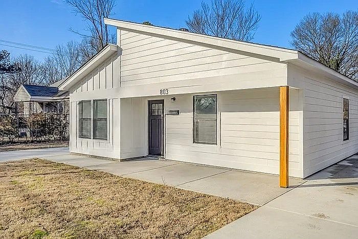A sleek modern bungalow featuring a white board-and-batten exterior, a unique asymmetrical roofline, and warm cedar accents.