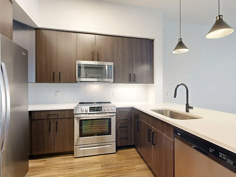 The kitchen features dark wood cabinets, stainless steel appliances, and a sink with pendant lights.
