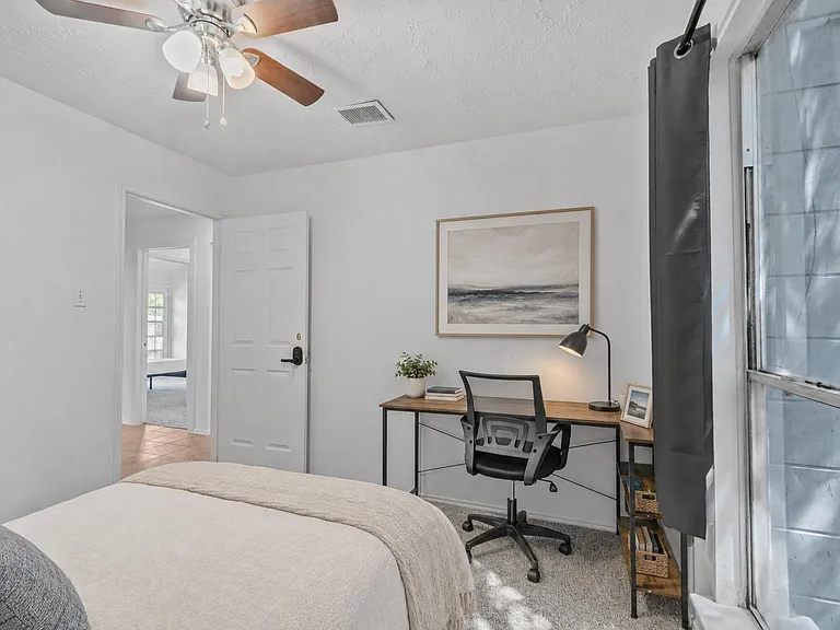 Bedroom with a full bed, dedicated desk setup, ceiling fan, and a large window for natural light.