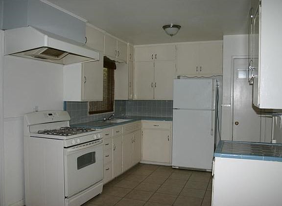 Retro kitchen with oversized ceramic tile flooring, refrigerator provided, large porcelain sink, hookup for washing machine in kitchen and hook up for dryer in carport.