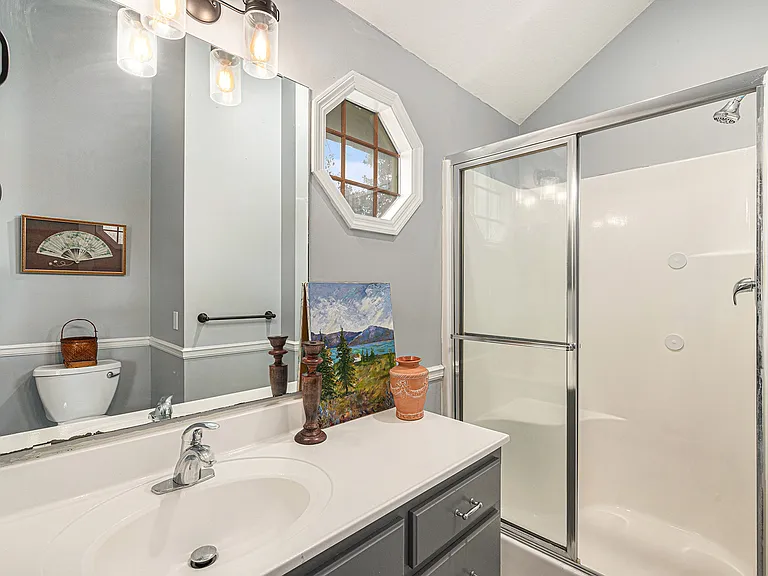 Refresh in this clean, all-white bathroom featuring a shower, toilet, and sink with a vanity mirror, offering a neat and comfortable space for your daily routine.