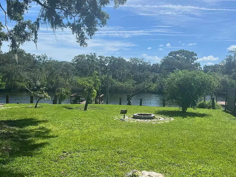 Spacious waterfront backyard with a grassy lawn, mature shade trees, and a private dockgreat for outdoor lounging.
