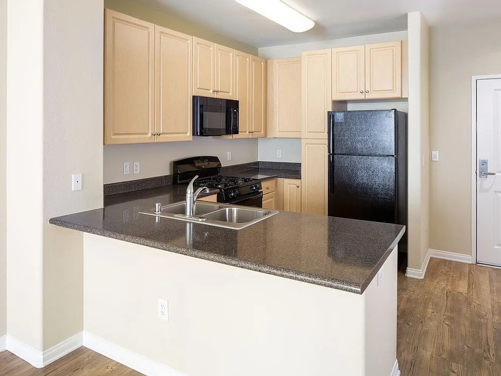 Kitchen with oak cabinetry, grey countertops, black appliances, and hard surface flooring - Avalon Warner Place