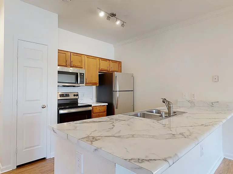 Apartment kitchen with stainless steel appliances, wood-style flooring, and marble-style countertops (shown here). Quartz-style countertops are available in select homes. Contact our team for details.