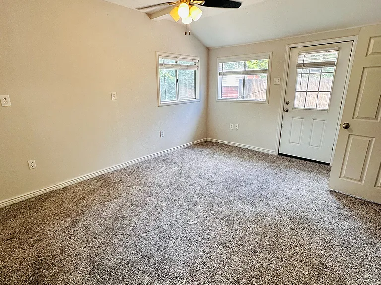 Bright and inviting room with plush carpet, ceiling fan, and ample natural light from large windows and glass door.