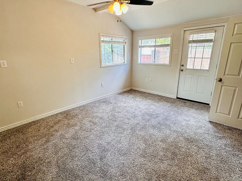 Bright and inviting room with plush carpet, ceiling fan, and ample natural light from large windows and glass door.