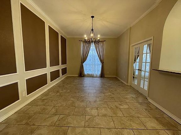 Empty room with plenty of natural light, ornamental molding, french doors, and an inviting chandelier