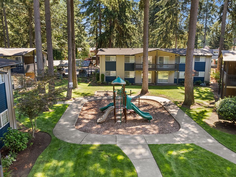 A beautifully landscaped apartment courtyard featuring a playground, mature trees, walking paths, and peaceful outdoor green space.