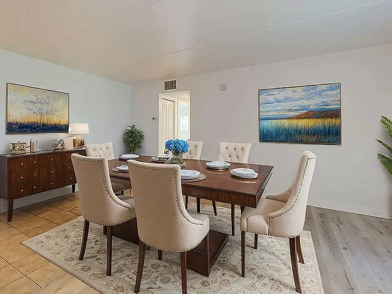 Sophisticated dining room featuring a polished wood table with elegant upholstered chairs, stylish artwork, and lush greenery creating a warm and inviting atmosphere.