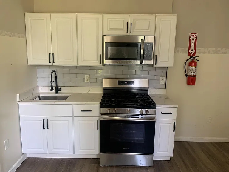 Streamlined kitchen with ample white cabinetry, subway-tile backsplash, and stainless steel range and over-the-range microwav
