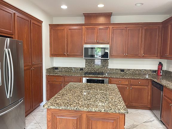 Kitchen full view showing stove and oven, microwave, refrigerator and cherry wood cabinets and a center island