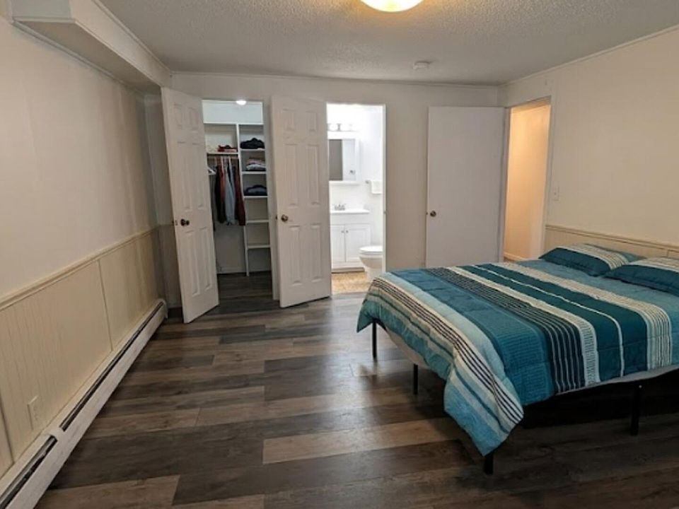 Spacious furnished bedroom with wood-look floors, a double bed, and an open closet area with shelving.