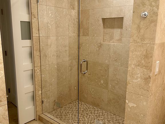 large shower for back bedroom with travertine stone and glass shower door
