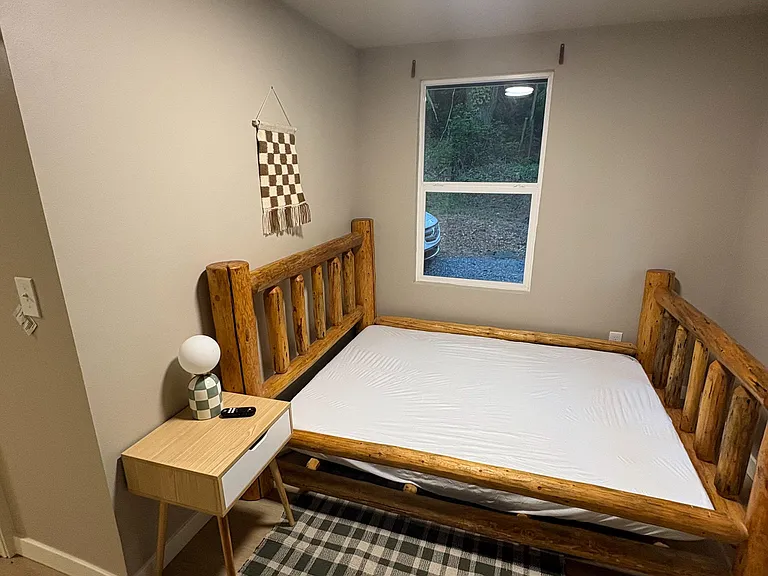 Furnished bedroom with a rustic wood bed frame, nightstand, and a window for natural light and outdoor views.