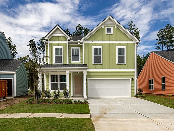 A green house with a white garage door is surrounded by other houses.