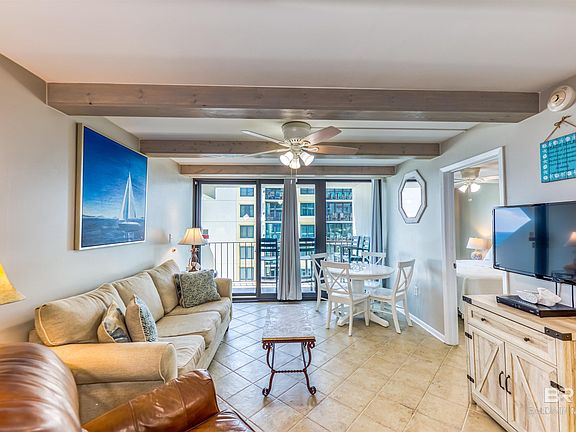 Living room with ceiling fan, light tile patterned floors, and beam ceiling