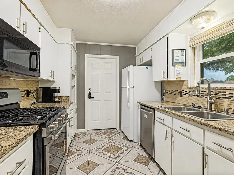 Galley kitchen with granite counters, ample cabinetry, gas range, microwave, dishwasher, and a double sink by the window.