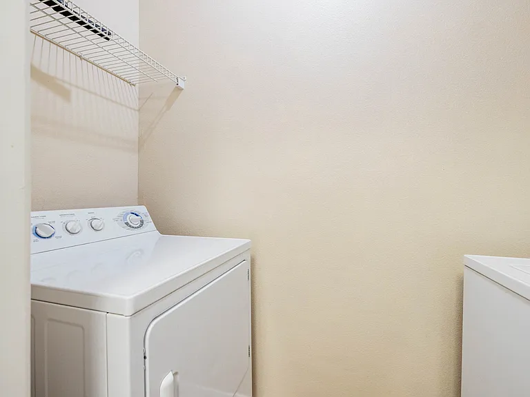 Bright and compact laundry room featuring a white washer and dryer with a convenient wire shelving unit. Bright and compact laundry room featuring a white washer and dryer with a convenient wire shelving unit.