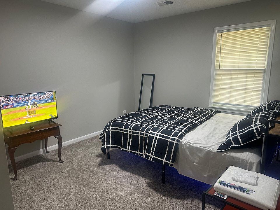 Furnished bedroom with a comfortable bed, carpeted floors, and a window with blinds for light and privacy.
