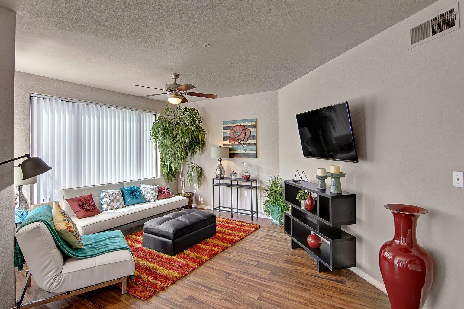 Living room with a sofa, ottoman, TV, and large plant.