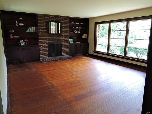 Spacious living room with wood burning fireplace sandwiched between built-in book cases and large windows showing view of the expansive backyard.