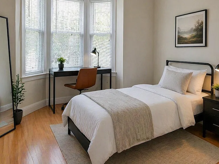 Bedroom with bay windows, full-size bed, nightstand lighting, and a dedicated desk area for work or study.