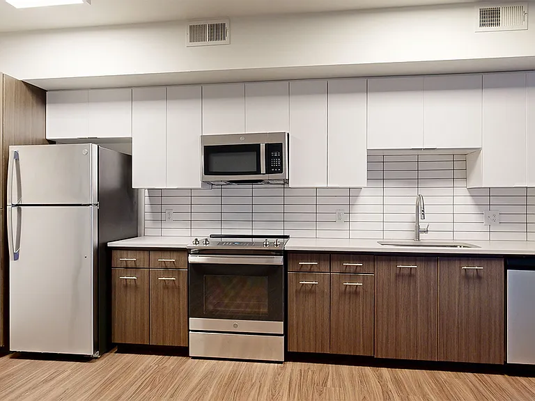 Apartment kitchen with stainless steel appliances, quartz countertops and wood-style flooring.