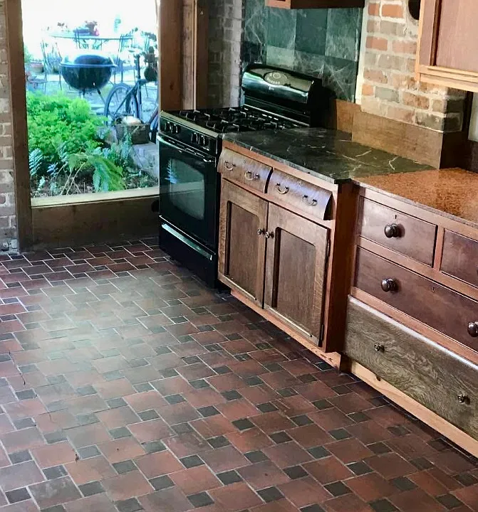 Kitchen with multiple windows and this one looks out onto the backyard gardens. Custom kitchen cabinets, exposed brick and tile floor. Gas stove.