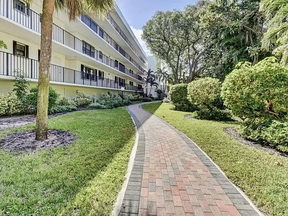 Back of the building with the pathway from the guests parking to the lobby between trees and flowers