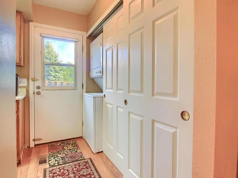 Full size stacked washer and dryer next to a large pantry, storage closet, and door to back patio.