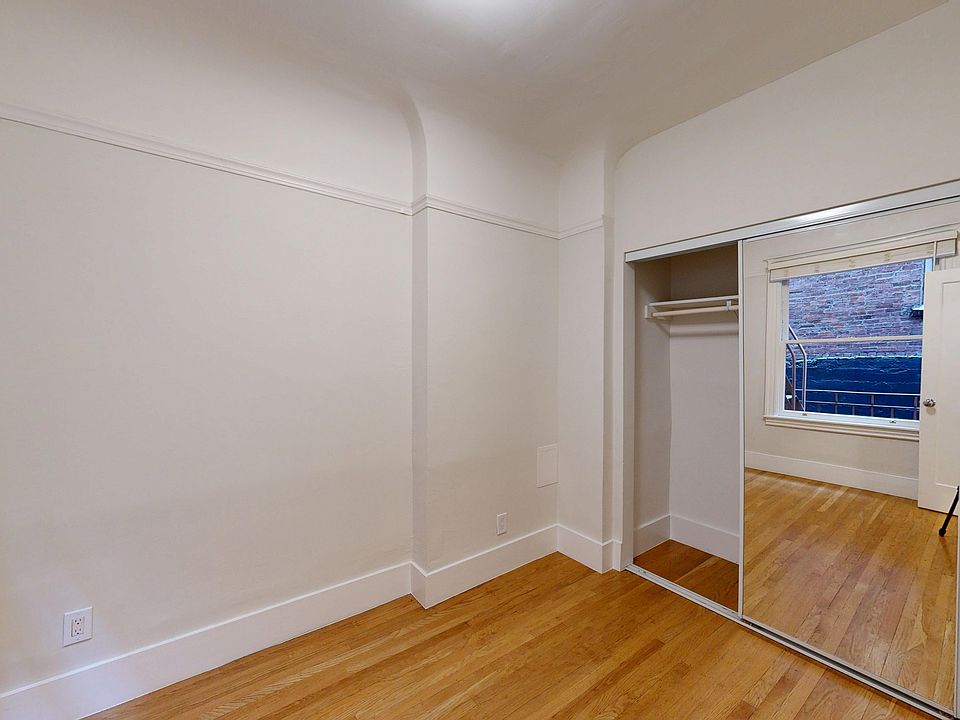 Bright room with hardwood floors, a mirrored closet, and a window revealing a brick exterior view