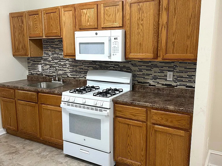 Eat-in kitchen with raised-panel oak cabinets, sandstone-style flooring & glass-bead backsplash