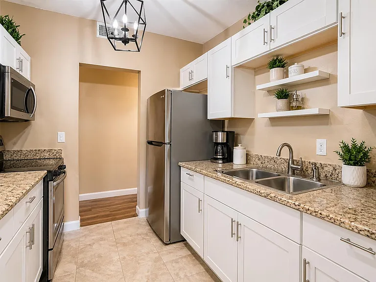 Galley-style kitchen with granite counters, double-basin sink, ample white cabinetry, and stainless steel appliances.