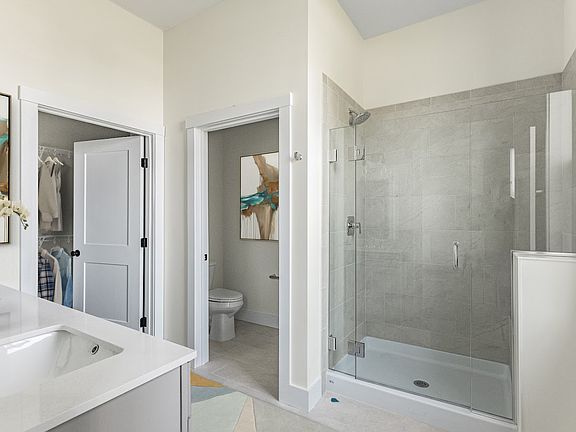 Modern bathroom with a glass shower stall, white cabinets, and a large mirror reflecting an adjacent