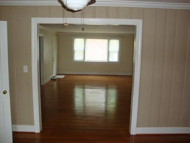 "3rd" bedroom view of living room with front entry door and large front window, kitchen entry door to left. Notice the hardwood floors.