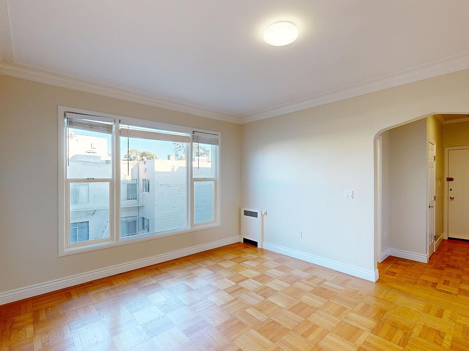 Spacious room with parquet floors, large windows, and a bright wall, featuring an arched doorway leading to the entrance.