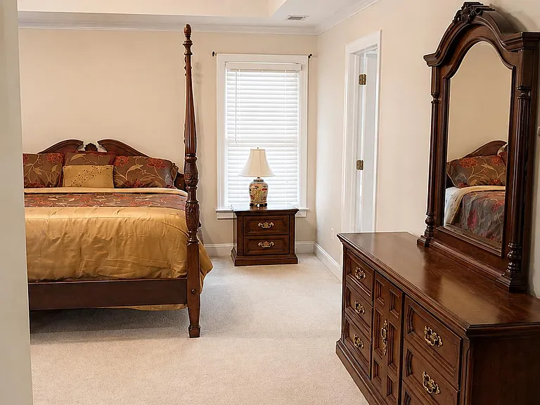 Spacious bedroom with a tray ceiling, ceiling fan, window blinds, and ample storage with a dresser and nightstand.