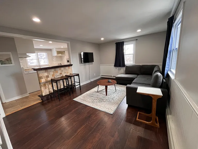 Open living area with sectional seating, wall-mounted TV, and a breakfast bar that connects seamlessly to the kitchen.