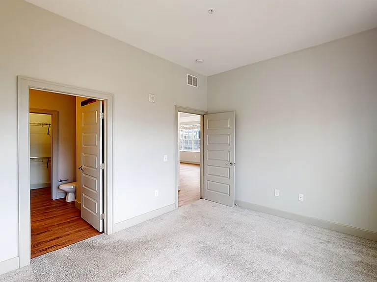Spacious apartment bedroom with attached bathroom and plush carpet flooring.